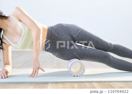 フォームローラーを使って太ももをほぐす女性 フォームローラーを使って太ももをほぐす女性 110704022