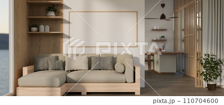 A modern, cosy living room with a couch in L-shape, a frame mockup on the wall, and decor. 110704600
