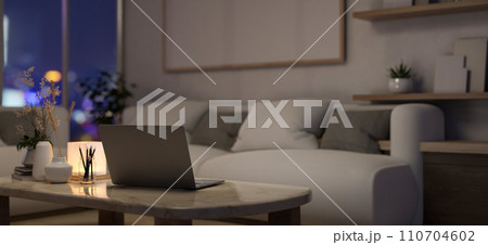 A laptop computer on a coffee table in a modern, cosy apartment living room at night. 110704602