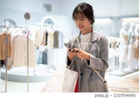A happy, pretty Asian woman is checking messages on her phone while walking in a shopping mall. 110704940