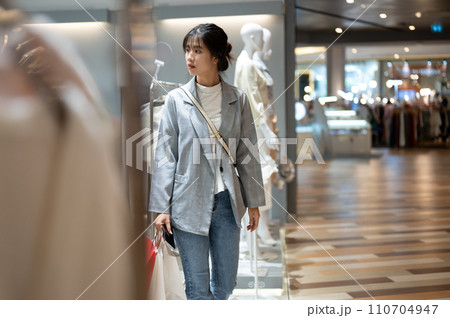 A beautiful young Asian woman in trendy clothes is walking in a shopping mall with her shopping bags 110704947