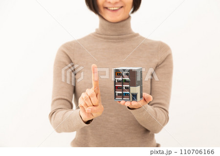 マンションの住宅模型を持って人差し指を立てるミドル女性 110706166