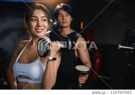 A fit couple in black workout clothes, smiling cheerfully while holding dumbbells, works together to build their muscular bodies and achieve their fitness goals. lifestyle fitness concept 110707083