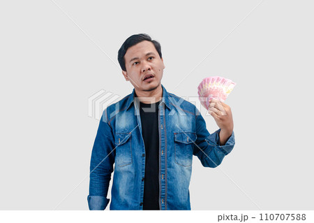 Young Asian man giving love symbol while holding paper money and showing happy expression Young Asian man giving love symbol while holding paper money and showing happy expression 110707588