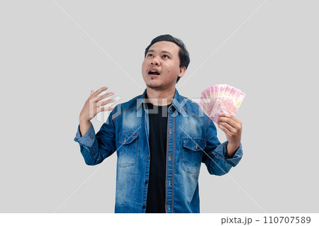 Young Asian man showing moved face expression while holding paper money 110707589
