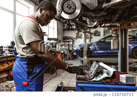 African male auto-mechanic repairing car brakes under the car in auto service 110710713