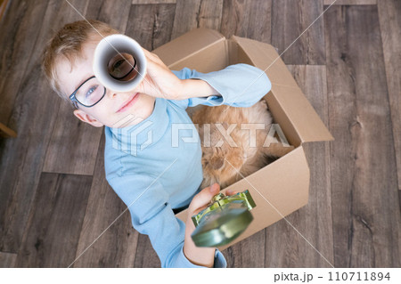 A small child, a boy, plays a pirate with a cat sitting in a box. Children's games in the children's room. Real friendship. 110711894
