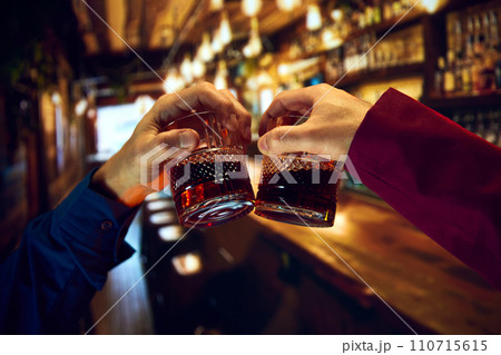 Male hands, businessmen clinking whiskey glasses, meeting at pub, restaurant. Friends meeting Male hands, businessmen clinking whiskey glasses, meeting at pub, restaurant. Friends meeting 110715615