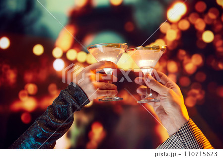 Romantic date. Mae and female hands clinking martini cocktails over bokeh background. Cheers. 110715623