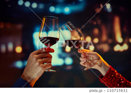 Anniversary celebration, Valentines day date. Male and female hands clinking glasses with red wine over restaurant background 110715631