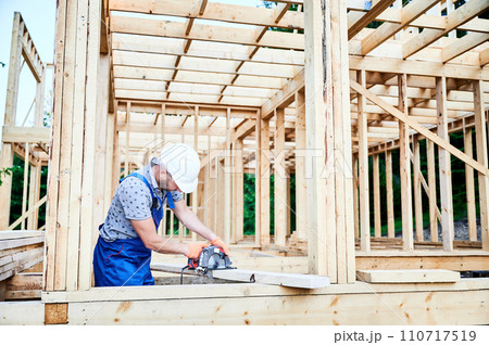 Carpenter using circular saw for cutting wooden plank. Man worker building wooden frame house. The idea behind modern ecological construction. 110717519