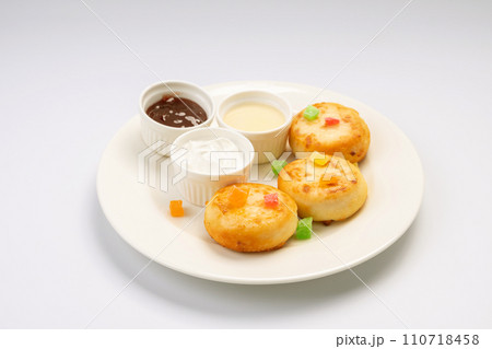 Breakfast. Cheesecakes with sauces and dried fruits on a white plate and a white background. 110718458