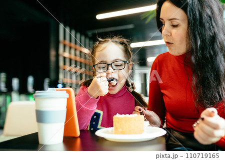 Happy family moments concept. Cute little daughter in eyeglasses and her mother eating cake at cafe together. Happy family moments concept. Cute little daughter in eyeglasses and her mother eating cake at cafe together. 110719165