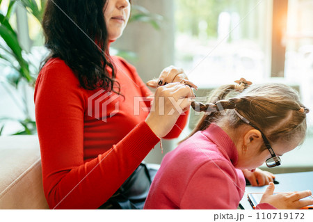 Happy family moments concept. Candid side view portrait of happy mother and daughter relaxing weave braids in cafe together and using smartphone. Happy family moments concept. Candid side view portrait of happy mother and daughter relaxing weave braids in cafe together and using smartphone. 110719172