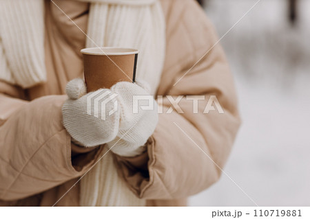 Female hands holding coffee hot drink cup and enjoys winter weather at snowy street close up 110719881