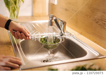Side view of human hand take a bunch of arugula and rinses with water Side view of human hand take a bunch of arugula and rinses with water 110720073