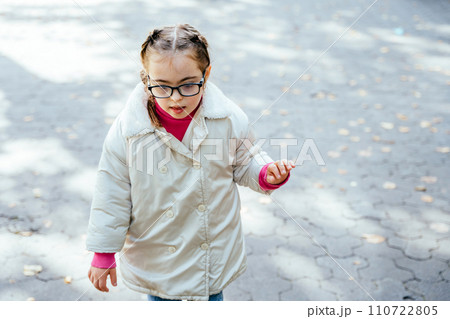 Focused child curious girl with two braids in eyeglasses, white coat smiling enjoying good sunny weather in autumn park outdoor. Focused child curious girl with two braids in eyeglasses, white coat smiling enjoying good sunny weather in autumn park outdoor. 110722805