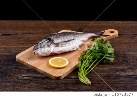 Dorado fish and a slice of lemon on a cutting board, a bunch of cilantro on the table. Dorado fish and a slice of lemon on a cutting board, a bunch of cilantro on the table. 110723677