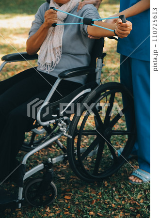 Young nurse or physiotherapist in scrubs helping a happy retired old woman do fitness exercises with light weight dumbbells at home. Concept of physiotherapy for seniors Young nurse or physiotherapist in scrubs helping a happy retired old woman do fitness exercises with light weight dumbbells at home. Concept of physiotherapy for seniors 110725613
