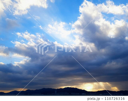 雲の隙間から降り注ぐ夕日の光と山のシルエット 雲の隙間から降り注ぐ夕日の光と山のシルエット 110726316