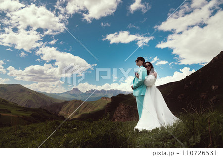 Happy wedding couple in the countryside. A wife hugs her husband from the back against the backdrop of green mountains 110726531