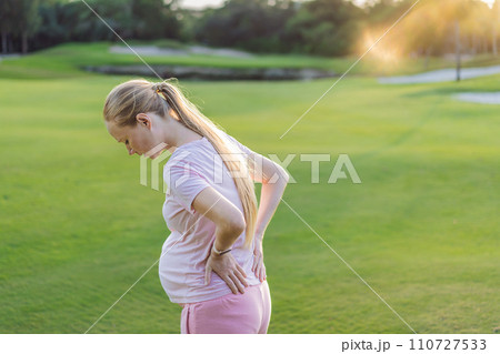 Expectant woman experiences back pain outdoors, seeking relief and comfort during pregnancy with a gentle outdoor stretch or rest Expectant woman experiences back pain outdoors, seeking relief and comfort during pregnancy with a gentle outdoor stretch or rest 110727533