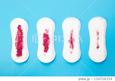 Feminine hygiene pads with red glitter on blue background. First menstrual period concept  110728154
