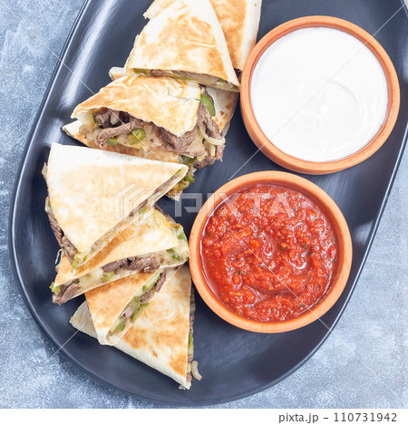 Mexican fajita quesadilla with pieces of beef steak, bell pepper, onion, cheese, top view square 110731942