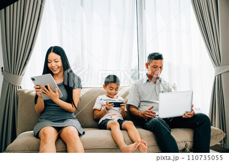 At home an Asian family's device obsession overshadows bonding time. Parents and kids immersed in gadgets illustrate the effects of excessive internet usage. ignores togetherness 110735055