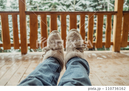 Woman legs in winter shoes - fur trendy boots on wooden balcony background. Woman legs in winter shoes - fur trendy boots on wooden balcony background. 110736162