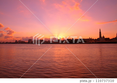 西ヨーロッパのベルギー アントワープを流れるエスコー川の対岸から朝焼けの市街地のシルエット 110737310