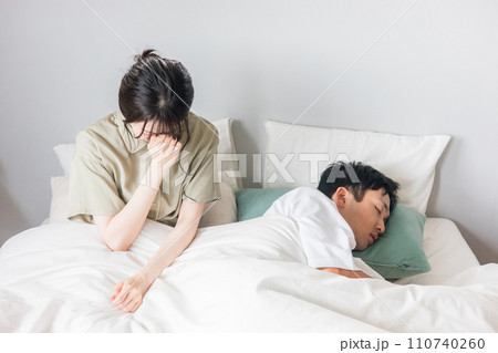 ベッドの上で睡眠不足に悩む女性と眠る男性 ベッドの上で睡眠不足に悩む女性と眠る男性 110740260