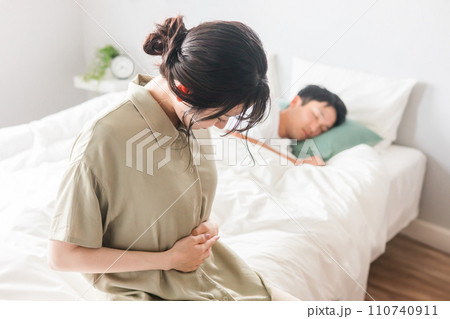 朝寝起きにベッドでお腹を抑える女性（妊娠・腹痛・つわり・妊活） 110740911