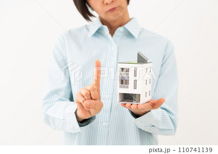 戸建ての住宅模型を持って人差し指を立てるミドル女性 110741139