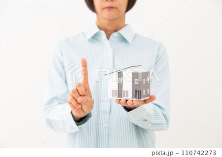 戸建ての住宅模型を持って人差し指を立てるミドル女性 110742273
