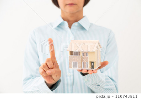 戸建ての住宅模型を持って人差し指を立てるミドル女性 110743811