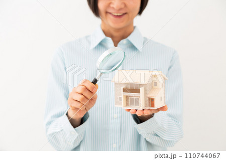 戸建ての住宅模型とルーペを持って微笑むミドル女性 110744067