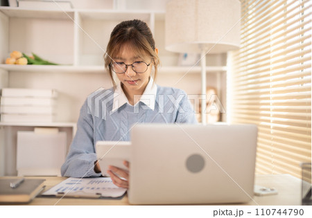 Woman working in front of laptop, Presses a calculator, Statistical graphs of investing in real estate, Finance, Accounting, Tex, Work for home. 110744790