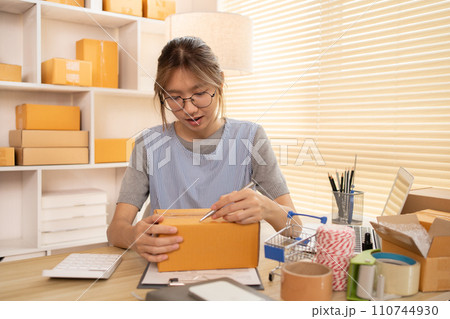 Sell products online, Woman is writing down the customer's details and addresses on box in order to prepare for shipping according to the information, Packing box, Sell online. 110744930