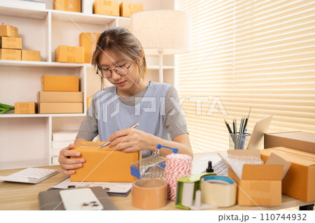 Sell products online, Woman is writing down the customer's details and addresses on box in order to prepare for shipping according to the information, Packing box, Sell online. 110744932