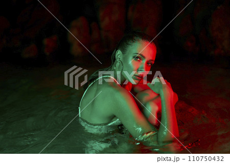 Woman immersed in water at night, illuminated by red and green lights, portrays solitude and reflection, possible depression or post-trauma calmness. 110750432