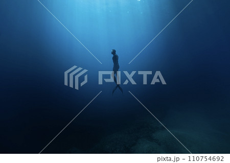 Freediver Swimming in Deep Sea With Sunrays. Young Man DIver Eploring Sea Life. 110754692