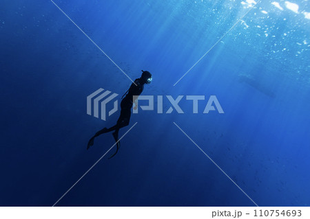 Freediver Swimming in Deep Sea With Sunrays. Young Man DIver Eploring Sea Life. Freediver Swimming in Deep Sea With Sunrays. Young Man DIver Eploring Sea Life. 110754693