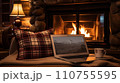 Laptop with a picture of a bonfire screen, indoor near burning fireplace in rustic style, with cozy blanket and cup of coffee. Seasonal remote work, internet, shopping. 110755595