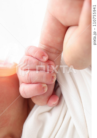 Close-up of baby's small hand, head, ear and palm of mother. Macro Photo of Newborn baby after birth tightly holding parents finger on white background. Family and home concept. Healthcare paediatrics 110755941