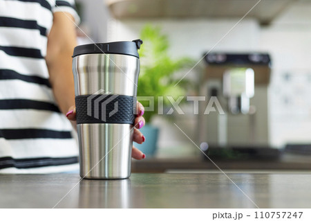 Hand Holding Stainless Steel Travel Mug in Kitchen 110757247