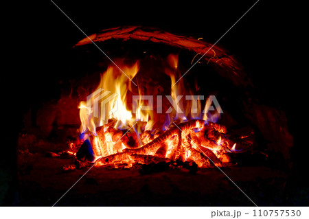 Flames dance above wood logs, casting a warm glow in the dark space. Flames dance above wood logs, casting a warm glow in the dark space. 110757530