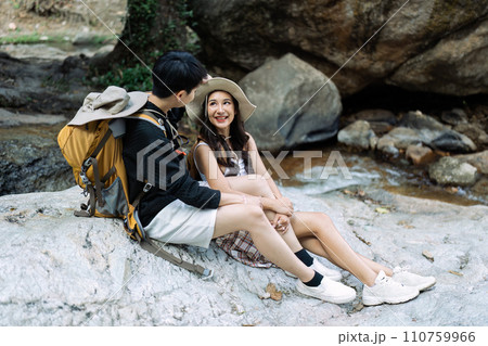 Lesbian couple relaxing together on rock at a hiking trail While traveling together on a hiking trail 110759966