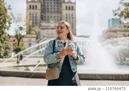 Young tourist woman walking in the park near Palace of Culture and Science in Warsaw city, Poland. Women chatting on cell smartphone while relaxing outdoors. Technology, Urban lifestyle concept 110760472