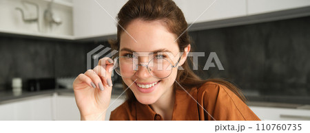 Close up portrait of happy, carefree young woman in her new glasses, showing her eyewear, laughing and smiling, posing in kitchen Close up portrait of happy, carefree young woman in her new glasses, showing her eyewear, laughing and smiling, posing in kitchen 110760735